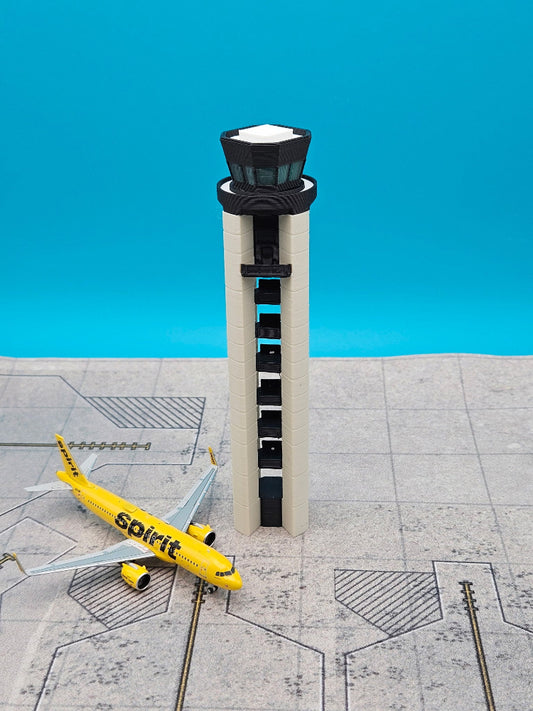 A miniature model of an airport control tower and a yellow Spirit Airlines plane on a gray runway diorama, set against a bright blue background.