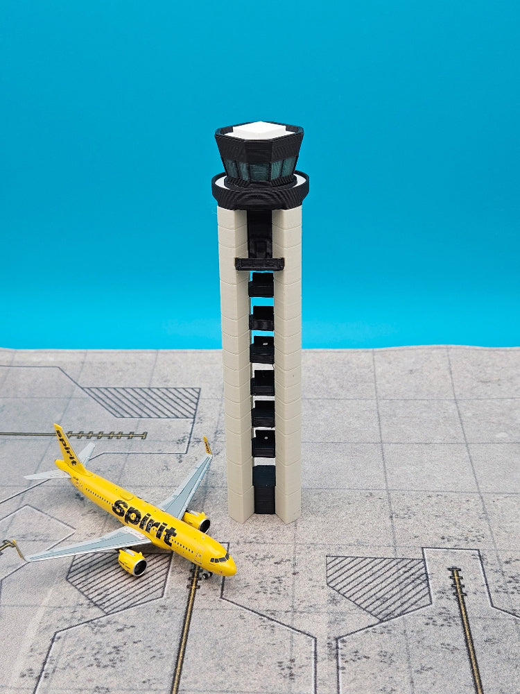 A miniature model of an airport control tower and a yellow Spirit Airlines plane on a gray runway diorama, set against a bright blue background.